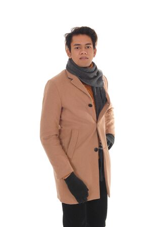 A handsome young man standing in the studio in a beige winter coat
and big scarf, looking into camera, isolated for white backgroundの写真素材