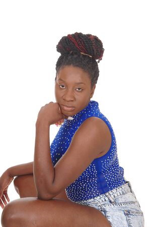 A gorgeous young African American woman crouching in profile on the
floor, in shorts and a blue top, isolated for white backgroundの写真素材