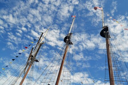 The tree masts of a large tall ship with there flags under a sonny skywith some white cloudsの写真素材