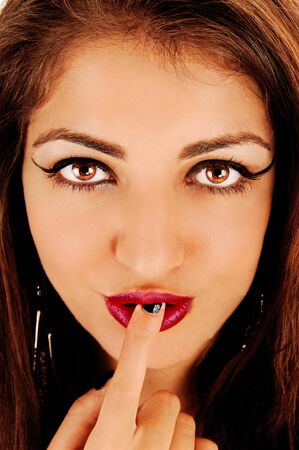 A gorgeous face of a young woman with big eyes and a finger in her mouthswith red lips looking at the cameraの写真素材