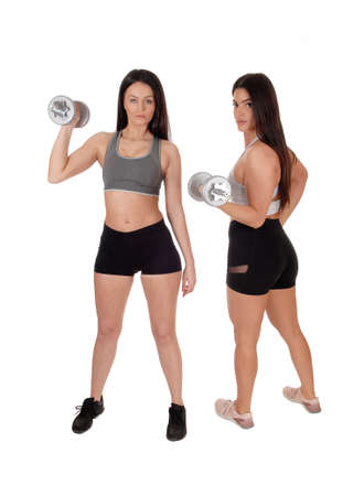 Two young beautiful woman standing in workout outfits in the studioworking out with there dumbbells, isolated for white backgroundの写真素材