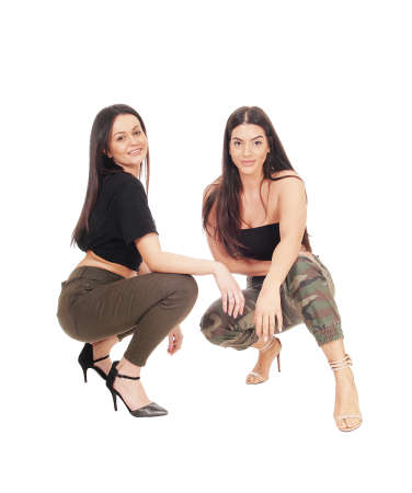 Two beautiful young woman crouching side by side in jeans and heels
looking at the camera, isolated for white backgroundの写真素材
