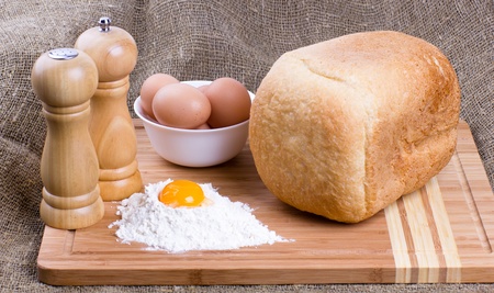 Yolk, eggs of house hens, salt, pepper and fresh hot home-made bread with wheat flour on kitchen to a boardの写真素材