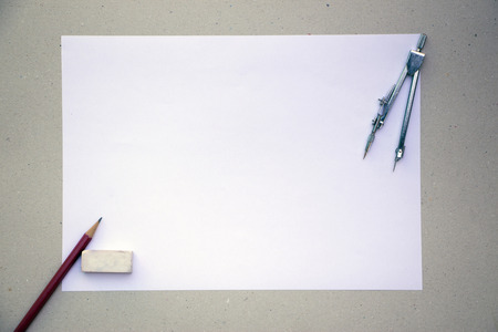 A blank A4 paper laid on a grungy, brown paper with metalic compass, red wooden pencils and a white rubber laid on the sidesの写真素材