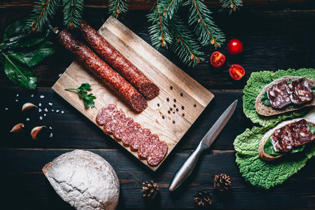 Smoked sausage on a wooden rustic table with addition of fresh aromatic herbs and spices, natural product from organic farm, produced by traditional methodsの写真素材