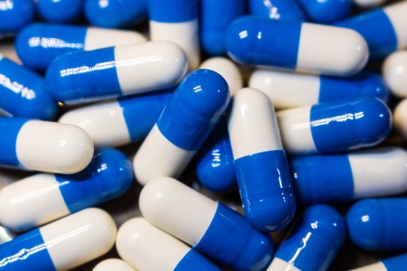 A handful of pills close-up. Capsules medications white and blue.