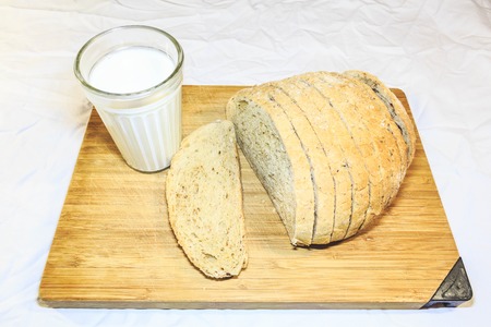 Bread cut into pieces on a wooden board next to a glass of milk too