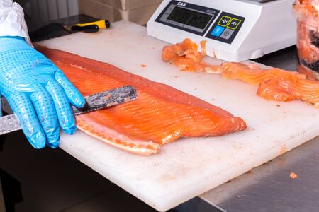 Fish production. A worker removes excess fat with a knife from a fish