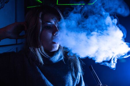 Asian girl exhales smoke from a hookah in blue tones.のeditorial素材