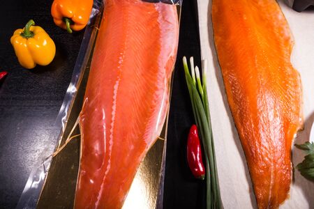Smoked fish next to lemon and vegetables tomatoes, onions, peppers and garlic