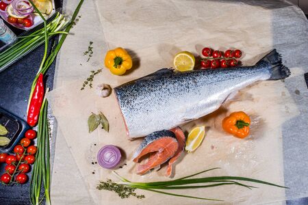 Salmon fish is a large piece and cut into pieces around vegetables pepper onions and lemon fruitの写真素材