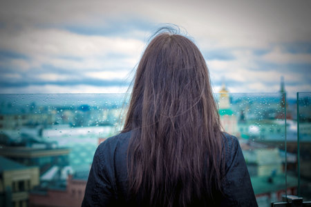 A brunette girl looks at the city from the roof of the house, rear viewの写真素材