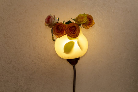 Warm light from a vintage wall lamp decorated with delicate roses in a cozy room atmosphere