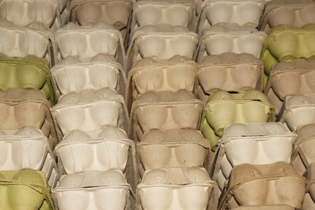 A large stack of empty cardboard egg containers in a warehouse for distribution and retail sale of...