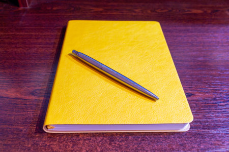 Bright yellow notebook and silver pen on dark wooden surface for creative writing ideasの写真素材