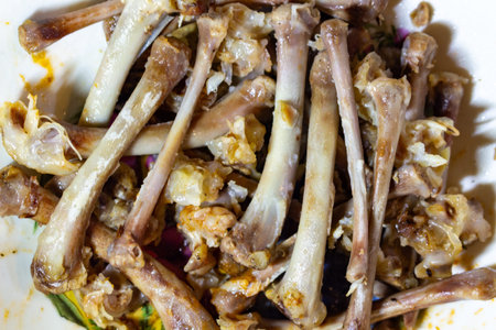 A pile of cooked chicken bones after dinner with spices and herbs on white plate