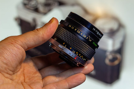 A hand holding a vintage fifty millimeter camera lens with focus ring detail