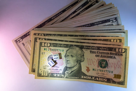 A stack of american ten and five dollar bills with dice on the foreground