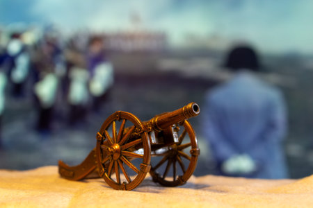 A miniature cannon model in front of a blurred historical battle scene with people standing