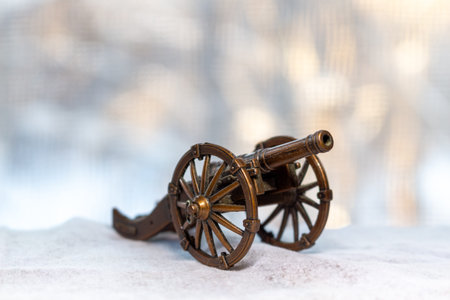 A miniature antique cannon on snowy surface with blurred winter forest background representing...
