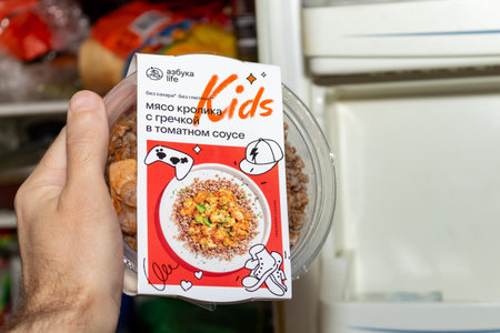 Hand holding prepared meal container with chicken and buckwheat in tomato sauce for children