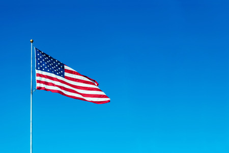 USA flag flies in a wind on blue sky background, place for your textの写真素材