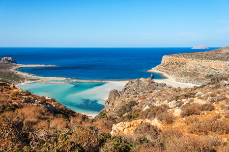 traveler with a backpack stands on a rock and looks at the panorama of the Balos beach, Crete,...