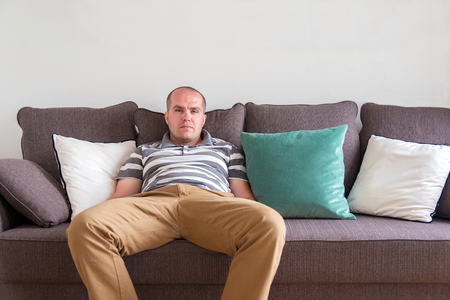 relaxed man sitting on the sofa and looking at the cameraの写真素材