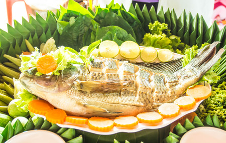 Close up a freshly steamed whole fish covered with herbs, onions and sauceの写真素材