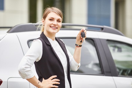 Woman holding keys to new car auto and smiling at camera.