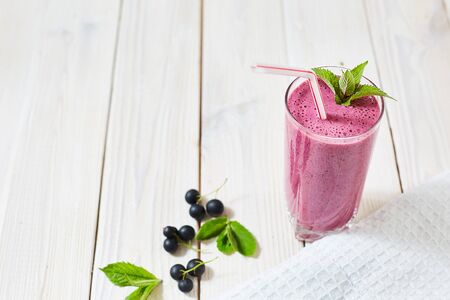 Vitamin Cocktail of blackcurrant berries, ice cream, milk in a glass cup. Plastic tube and mint. Wood white background and dishcloth. Horizontal image with copy space. Minimalism. Healthy eating concept.の写真素材
