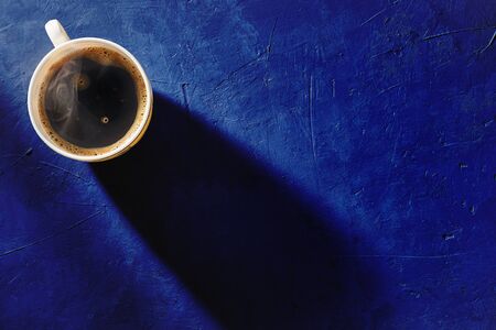 Coffee cup on blue background, top view. Morning shadow from a cup on a concrete table. Stylish design. Copyspace.の写真素材