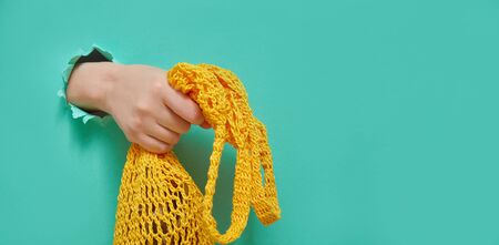 Eco mesh string bag in woman's hands from a round hole in green paper. Trend banner for any store or...
