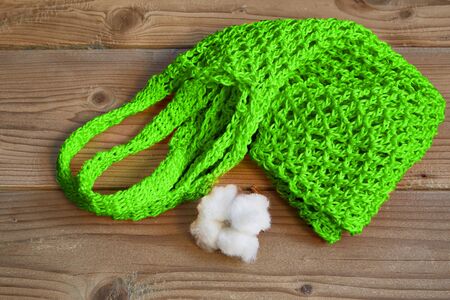 Green string bag and cotton boll lie on a wooden brown background.