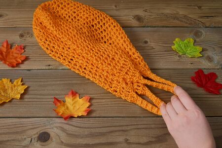 Orange string bag on a wooden background with autumn leaves around. Zero Waste shopping concept.
