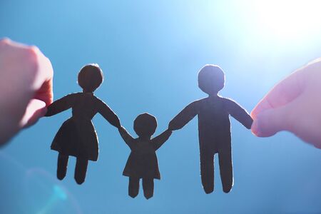 The concept of a happy family. Children's hands hold paper figures of mom, dad, baby on a background...
