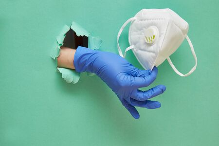A hand in a protective blue glove holds a mask to protect the respiratory system and face. Hole in...
