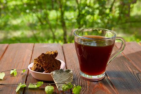 Cup of chaga tea on a dark table. Slices of natural and wild chaga mushroom and a sprig of birch.の写真素材