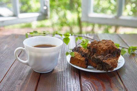 Chaga mushroom and a cup of chaga tea on a wooden surface next to an open window on a sunny summer day. A healing and healthy drink that helps with cancer.の写真素材
