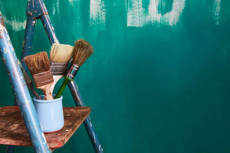 Background for text about repair and wall painting in the apartment. Tassels and stepladder on a green background.の写真素材