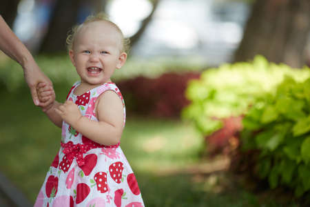 Little girl of one or two years old in a multi-colored dress holds an adults hand and laughs merrily. Three teeth in the mouth. Close-up with space for text.の写真素材