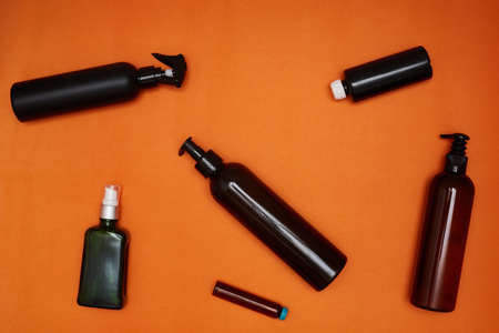 Creative flat lay of dark cosmetic bottles on a bright orange background.の写真素材
