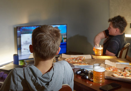 Guys  night. Two men are watching TV, drinking beer and eating pizza.の写真素材