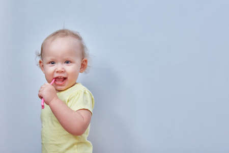 Toddler brushes his teeth against a light background. Copy space