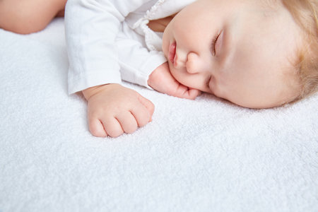 Cute baby sweetly sleeps on white bed linen in white clothes. Close-up. Beautiful healthy soft skin, long eyelashes. Space for the text.の写真素材