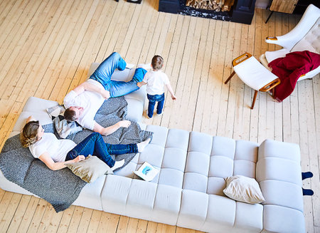 A family with a small child is relaxing on a huge gray sofa in the living room. Lifestyle. Family look in jeans and white T-shirts. Top viewの写真素材
