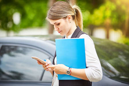 A young business woman with a folder for papers in her hands looks at her smartphoneの写真素材