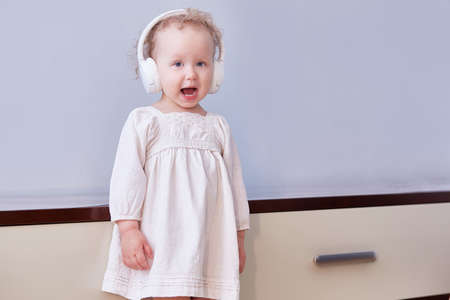 Little girl sings a song in her headphones. Light background with space for textの写真素材