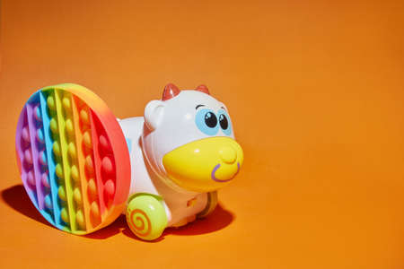 Baby kids toys orange background with copy space. Multi-colored rainbow pop can reduce stress and anxiety in children and adults. Plasmassovaya cute cow.の写真素材