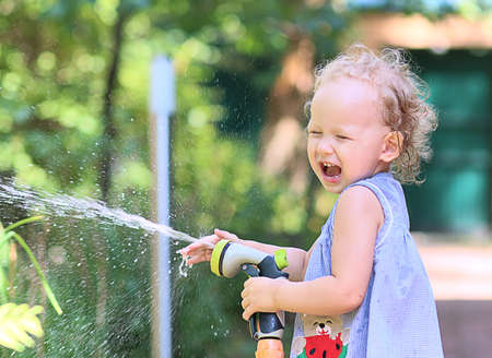 little girl cheerfully splashes water from a watering hose on a sunny summer dayの写真素材